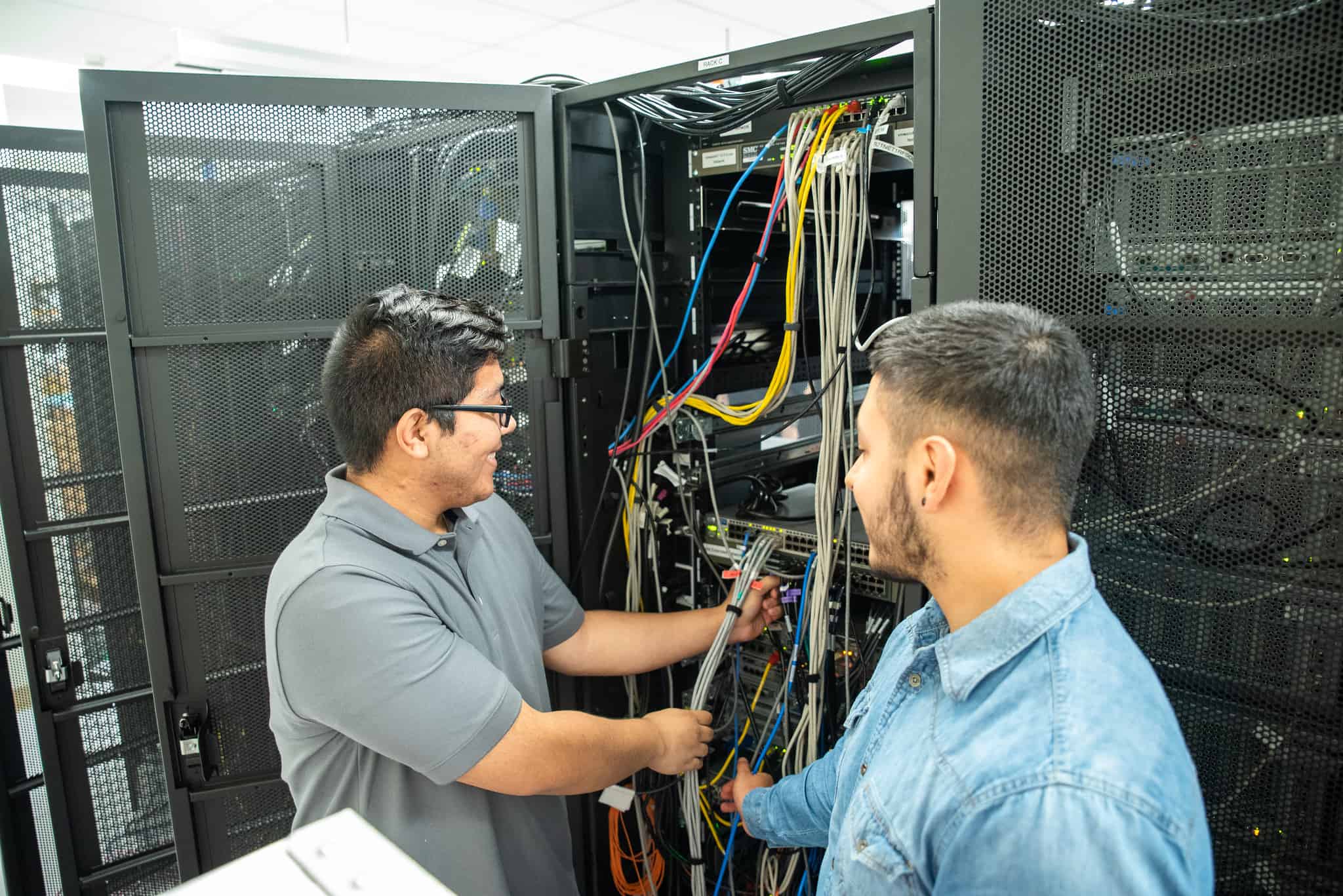 Dos estudiantes varones de P-TECH trabajando con cables de red durante sus prácticas en IBM.