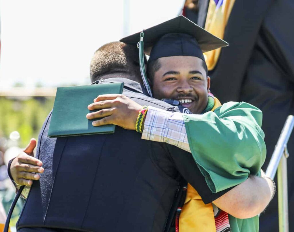 Un estudiante de último curso sostiene su diploma y abraza a un agente de recursos escolares