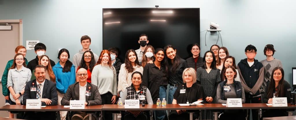 Grupo de estudiantes y profesionales médicos de UCHealth posando para una foto en el Panel de Salud. 