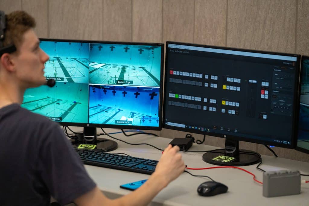 Student in front of monitors depicting underwater robotics field. 