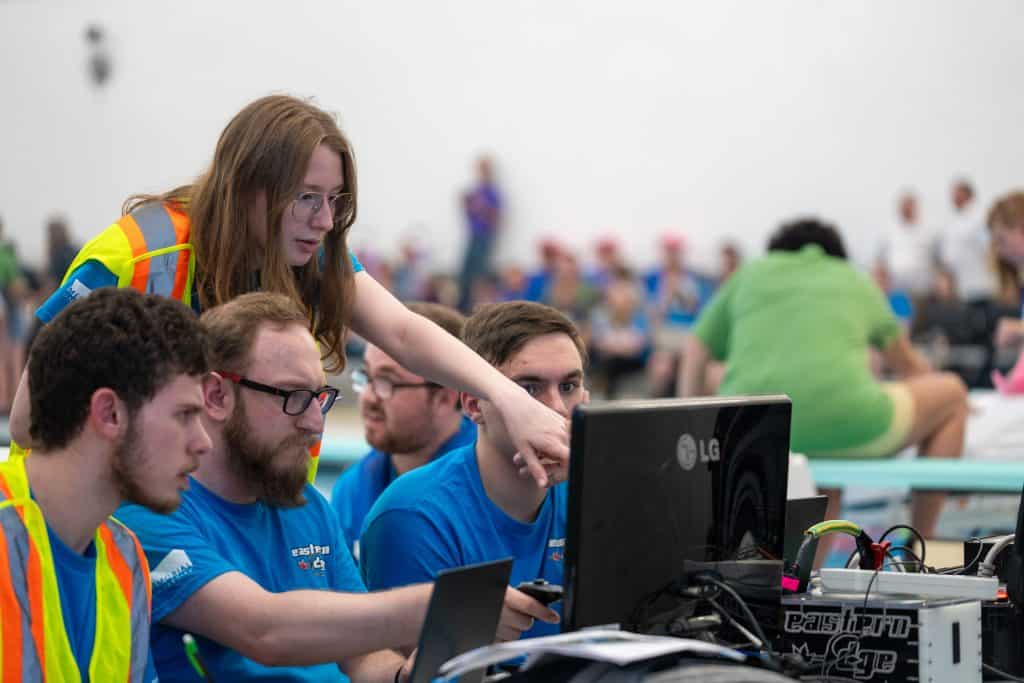 A group of students point to monitors as they watch the underwater robotics competition live stream.