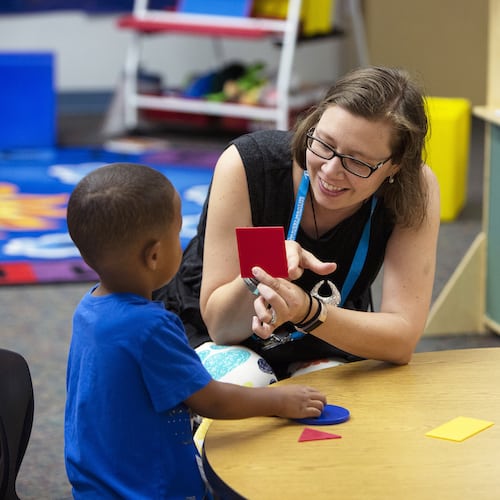 Teacher holding up card to student in preschool classroom.