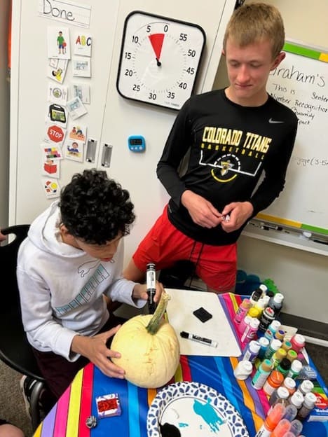 Student painting a pumpkin, while their "buddy" watches them