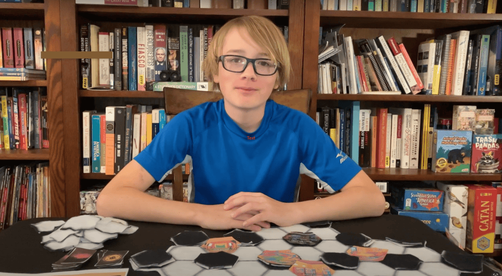 7th grade boy Wolf Danzer sitting at a desk with his arms crossed on top of his game which is on the table in front of him. 