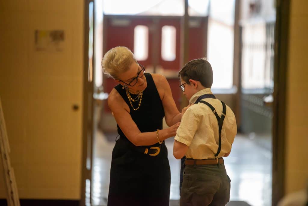 Female teacher helps a male middle school student tie his tie in the hallway. 