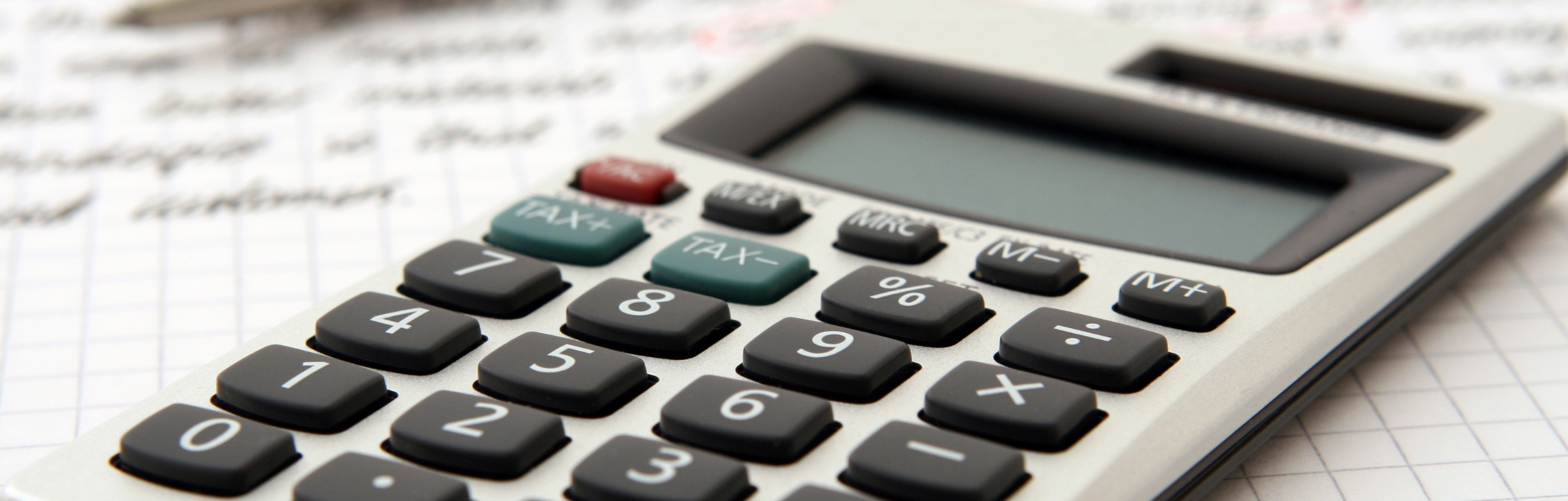 A close-up of a calculator on a graph paper background with handwritten notes visible.