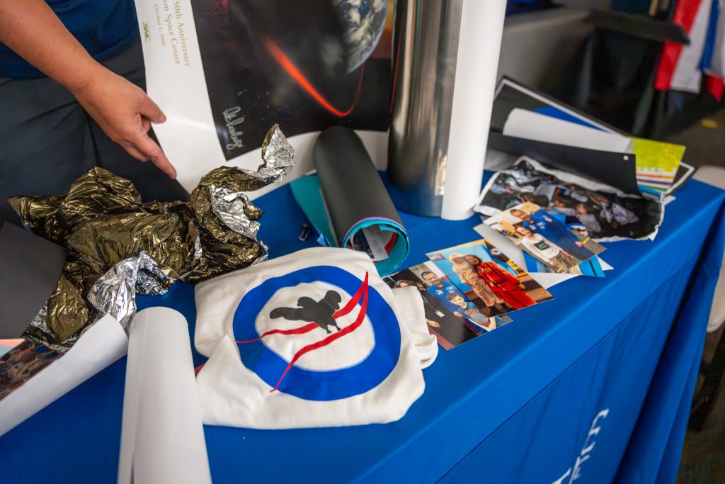 A table covered with various items, including a poster, photos, a T-shirt with a logo, and crumpled foil.