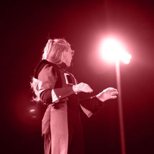 A performer in a stylish outfit gestures under bright stage lights, creating a dramatic atmosphere.