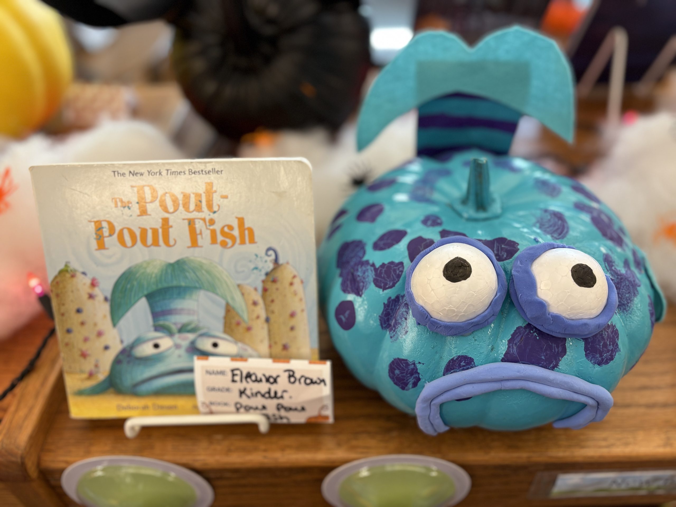 A blue pumpkin decorated as the Pout-Pout Fish next to the book "The Pout-Pout Fish," with a name tag.