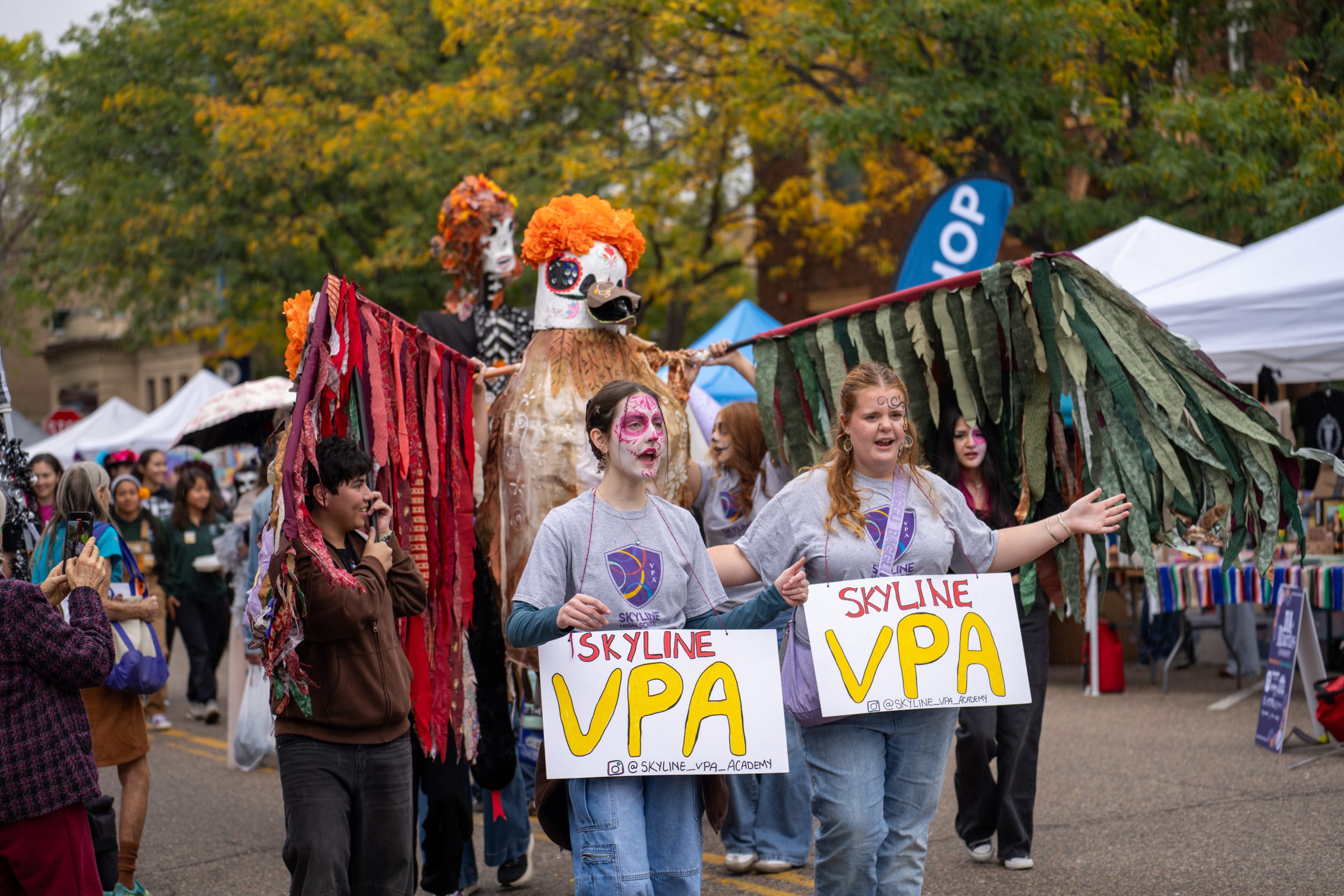 Participants in costumes march in a parade, holding signs for "Skyline VPA" amidst a festive atmosphere.