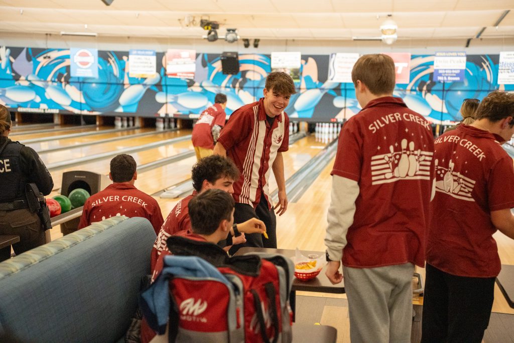 A group of young bowlers in red shirts at a bowling alley, enjoying snacks and chatting near the lanes.