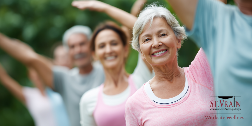A group of smiling adults participate in an outdoor wellness exercise class, stretching with arms raised.