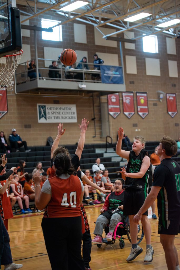 A basketball is in mid-air as players from both teams reach for it during a game in a gymnasium.