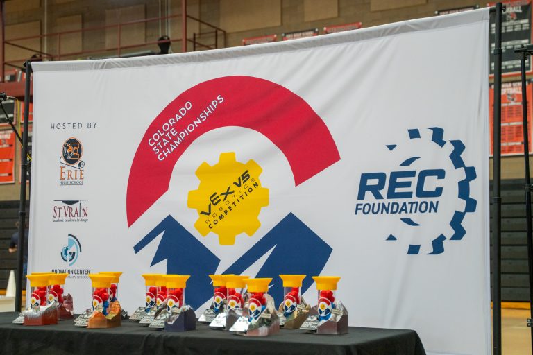 Banner for the Colorado State Championships featuring VEX Robotics logos and colorful trophies on a table.