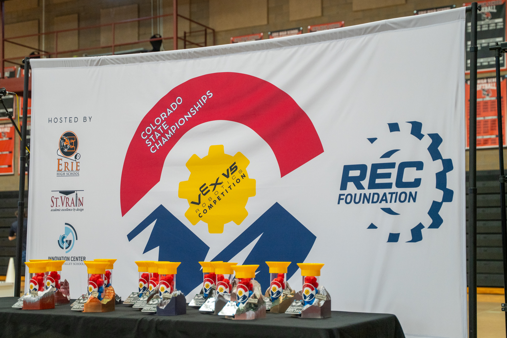 Banner for the Colorado State Championships featuring VEX Robotics logos and colorful trophies on a table.