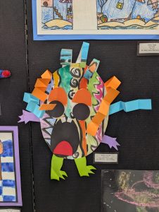 Colorful paper monster craft with large eyes, wild patterns, and limbs in various colors, displayed on a black background.