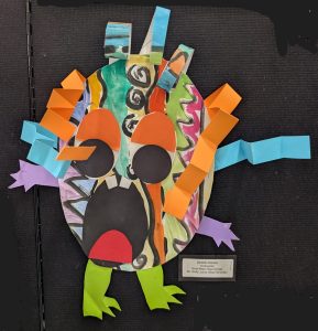 Colorful paper monster art with large eyes, vibrant details, and playful limbs, displayed on a black background.