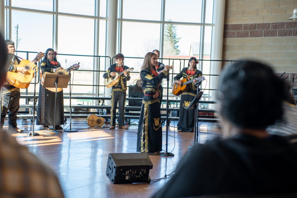 A mariachi band performs in a sunlit venue, featuring musicians with guitars and traditional attire.