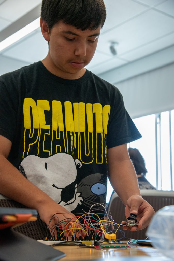 A young person in a black "Peanuts" shirt works with colorful wires and components on a table.