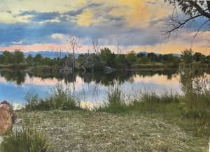 Serene lake scene at sunset, with reflections on the water and lush greenery along the shore.