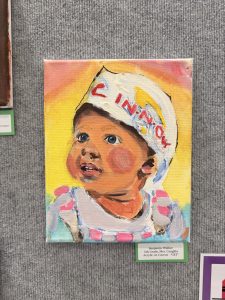 A colorful painting of a baby wearing a white hat with "CIN" on it, gazing upwards with a joyful expression.
