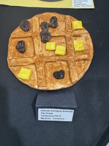 A ceramic waffle sculpture with yellow and black pieces, displayed on a black surface, labeled with artist details.