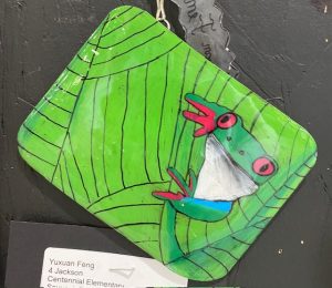 A colorful frog illustration on a leaf background, displayed on a rectangular piece of art.