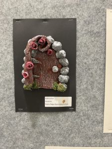 A decorative wooden door surrounded by stones and roses, displayed as a school art project.