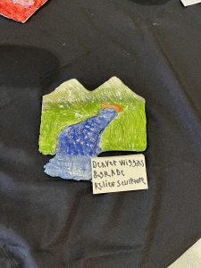 A colorful relief sculpture depicting mountains and a river, labeled with the artist's name and grade.