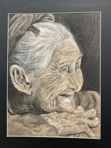 A close-up portrait of an elderly woman with deep wrinkles, white hair, and a warm smile, resting her chin on her hands.