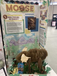 A school project display featuring a moose sculpture, with illustrations of nature and educational text about moose.