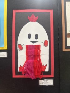 A colorful drawing of a chicken with yarn for a scarf, displayed on a black background with a red border.