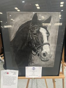 A charcoal drawing of a horse's head, framed with an award certificate for excellence in art displayed below it.