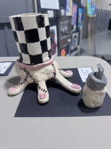 A checkered ceramic cup with a pink base sits beside a small gray and white bottle on a dark background.