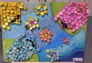 Colorful paper art featuring flowers and fish shapes in various colors arranged on a blue and green background.