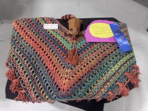 A colorful crocheted handbag with tassels, accompanied by a "Do Not Touch" sign and a blue ribbon award.