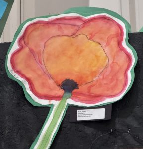 A colorful watercolor painting of a poppy flower with a green stem, displayed on a black background.