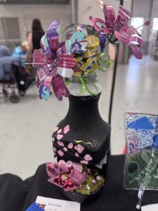 A decorative bottle features colorful, crafted flowers made from paper, with painted details and embellishments.