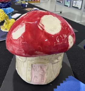 A ceramic mushroom sculpture with a red cap and white spots, featuring a small door at the base.