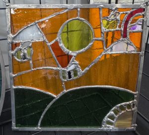 Colorful stained glass panel featuring geometric shapes in orange, green, and white, framed in metal.