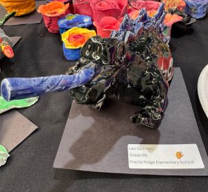A ceramic sculpture of a dinosaur with a long blue tongue, surrounded by colorful clay flowers.