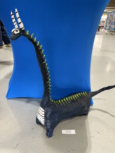 A colorful, handmade dragon sculpture with a long neck, green spikes, and a blue background.