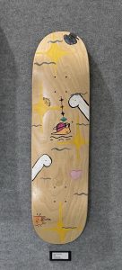 A skateboard deck with colorful abstract designs, including whimsical characters and stars on a wooden surface.