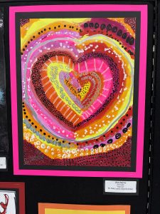 A colorful heart artwork with concentric patterns in pink, orange, and yellow, framed in bright pink and black.