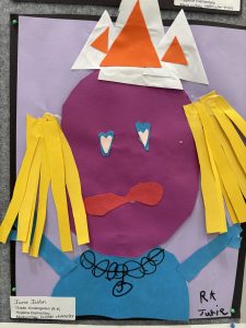 A colorful collage of a character with a purple face, orange crown, yellow hair, and blue shirt, made from paper.