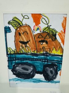A colorful drawing of two smiling pumpkins in a blue cart, with a rainbow and leafy details in the background.