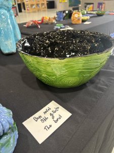 A glossy green bowl with a black interior sits on a table, accompanied by a label indicating its creator and grade.