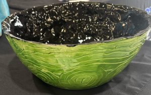 A decorative bowl with a textured green exterior and a shiny black interior, placed on a dark surface.