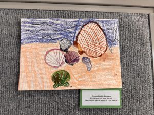 Colorful drawing of seashells on a sandy beach with blue waves and birds in the sky, titled "The Beach."