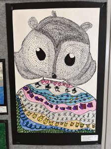 A colorful drawing of an owl with large eyes, wearing a patterned scarf featuring hearts and various designs.